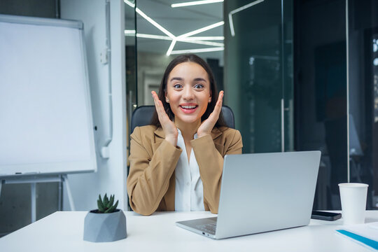 Cheerful business woman celebrating professional success, working at laptop, laughing, shouting for joy at office workplace, getting good news from video call