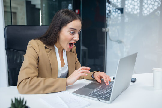 Surprised shocked businesswoman looking at laptop screen at office. Pretty girl suddenly excited with e-mail or news on Internet. Get promoted with salary increase.