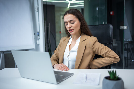 Woman with hip, back, spine spasm, cramp and pain, working from office troubles and issues.incorrect posture concept. frowning woman sitting at desk in front of laptop