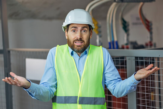 Handsome man with beard wearing safety helmet and reflective jacket clueless and confused with open arms, no idea and doubtful face.