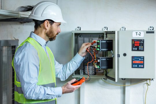 Electrician engineer work tester measuring voltage and current of power electric line in electrical cabinet control.