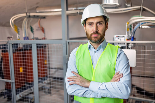 Assured male technician in a switchboard room crossing arms in an electrical substation setting. Portrait of professional electrician.