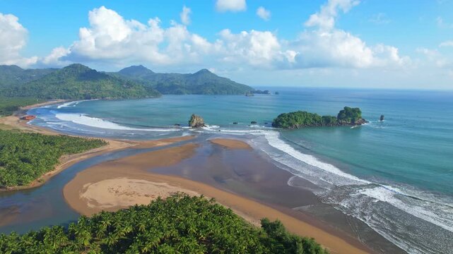 Aerial close up drone footage of Panggul beach bays, in Trenggalek regency, Java island, Indonesia, with beautiful cream sand, a small rock and small island, cliffs behind, turquoise sea at sunset