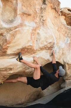 Climber reaching on overhang boulder in Joshua Tree desert
