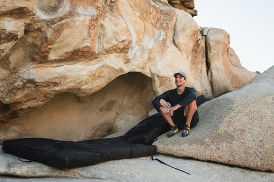Smiling climber resting by boulder with crash pads in desert