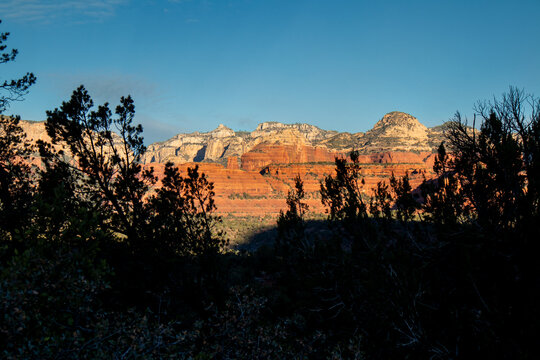 Sunlit red rock cliffs above desert valley with silhouetted trees