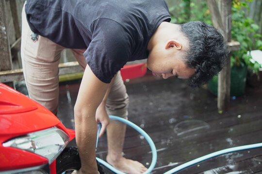 Young Asian man washing and wiping a red scooter at home backyard