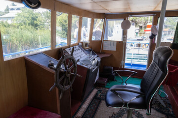 Interior of small passenger boat captain cabin with wooden helm, control panel and chair, moored near shore on Issyk-Kul lake in Kyrgyzstan, daylight through windows. © lucky pics