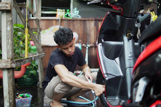 Young Asian man washing and wiping a red scooter at home backyard