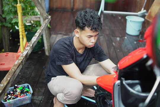 Young Asian man washing and wiping a red scooter at home backyard