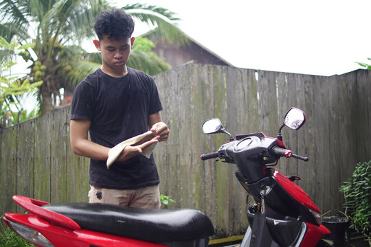 Young Asian man washing and wiping a red scooter at home backyard