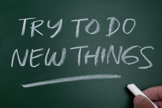 Hand writing inspirational quote 'Try To Do New Things' on a green chalkboard
