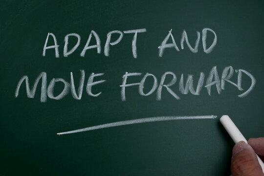 Hand writing motivational quote 'Adapt and Move Forward' on a green chalkboard
