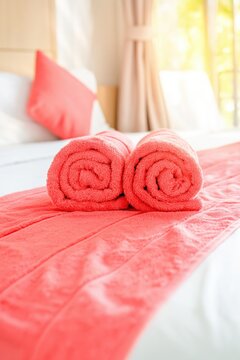 Two rolled coral towels on matching runner across bed room