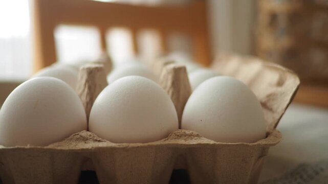 Close up of fresh white chicken eggs in carton box on table, cinematic motion footage.