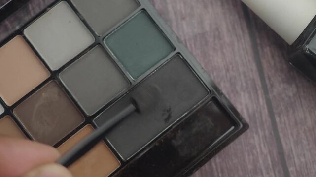 Applying dark eyeshadow with sponge applicator on makeup palette, beauty product close up.