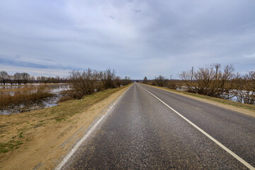 Naklejka premium Long asphalt road stretches straight ahead through wetlands