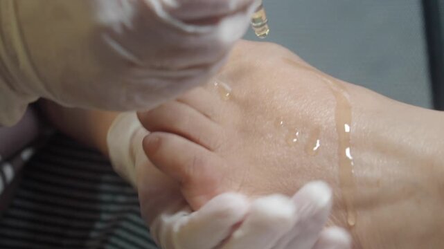 Professional podiatrist applying therapeutic oil on female foot during pedicure procedure.