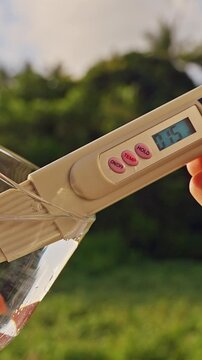 First Person View Of Hands Measuring Drinking Water With Digital Quality Meter Showing Fifteen Ppm In Glass With Tropical Forest Background. Water Purity Monitoring, Healthy Lifestyle