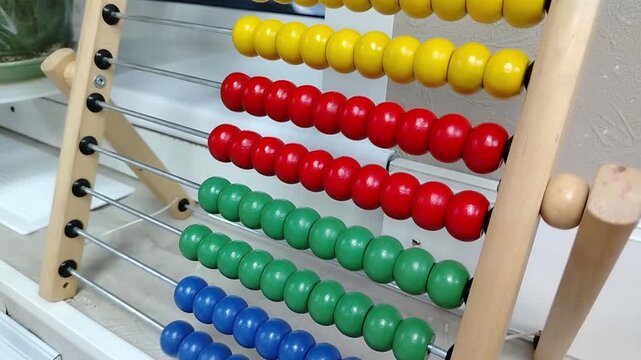 Colorful wooden abacus with red, green, yellow, and blue beads arranged on rods, showcasing a gradual shift in bead positions across three frames in a bright indoor setting