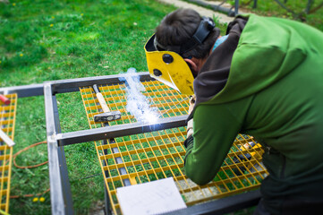 Worker uses welding equipment on metal frame in outdoor setting during daytime in a construction area