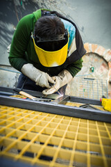 Worker uses welding tool on metal surface in a workshop during daylight hours for maintenance or repair tasks