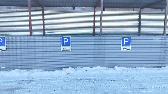Snow-covered parking area with visible parking signs and metal wall, showcasing gradual changes in the scene across three sequential frames in a winter setting
