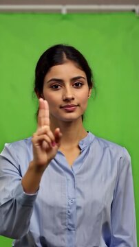 South Asian young adult female teacher on green screen raises one finger to signal wait with calm authority for classroom control instruction patience or service pause scenes indian woman