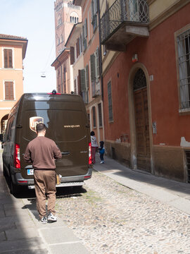 UPS courier delivering packages from a brown Mercedes Benz Sprinter van on a historic cobblestone street in Italy