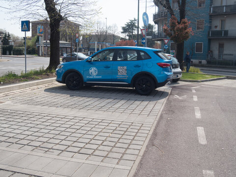 Blue MG EHS plug in hybrid SUV parked on interlocking pavement with Gruppo Bossoni branding and visible QR code for marketing