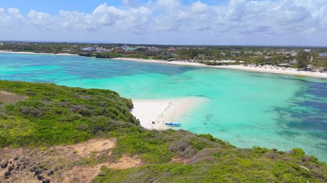 Aerial view of turquoise ocean water and white sandbanks surrounded by green coastal cliffs and village buildings at Watamu Beach, Kenya.