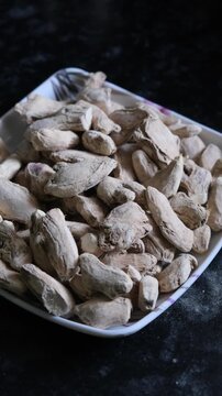 High angle view of dried ginger roots piled in a white square plate on a dark surface