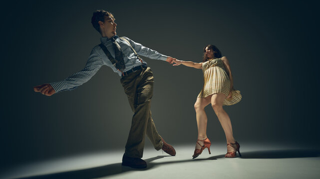 Retro style couple dancing lindy hop in studio with dramatic lighting expressive motion. Concept of vintage lifestyle, artistic performance, partnership trust, creative movement, rhythm expression.