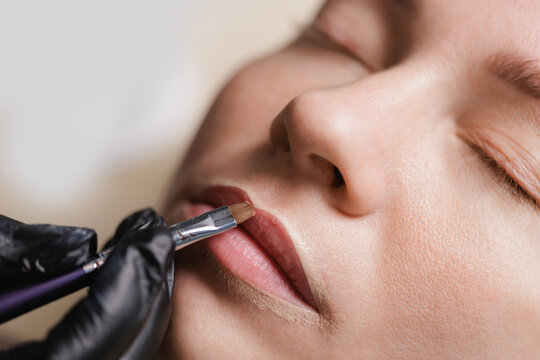 Woman having lip makeup applied in closeup beauty setting, application of permanent makeup contour