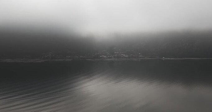 Aerial view of houses on the water's edge, shrouded in ethereal mist, creating a captivating contrast, Terunyan, Bali, Indonesia.