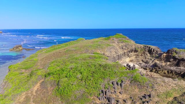 Aerial view of rocky cliffs covered in green vegetation overlooking the turquoise Indian Ocean with a boat at Watamu Beach, Kenya.
