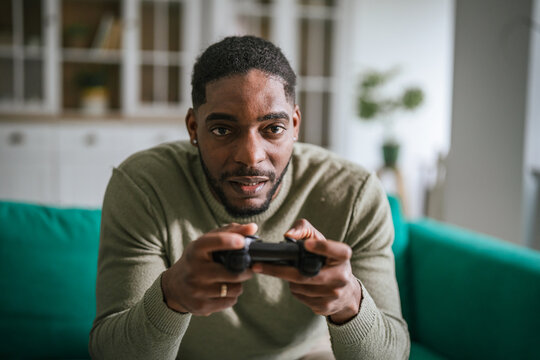 Black man holding controller playing video game at home