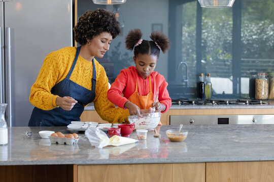 Mixing Diverse mother and daughter at marble countertop in home kitchen, using glass mixing bowl