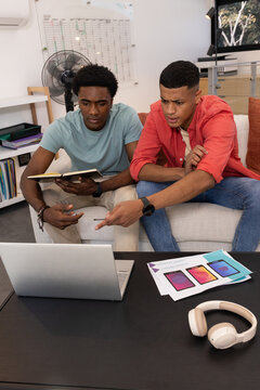 Leaning Diverse male coworkers checking laptop screen in lounge area, with notebook and mockups