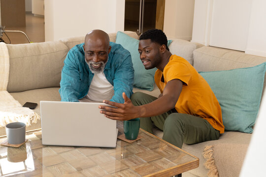 Sitting African American father and son focusing on laptop in living room, with mugs and smartphone