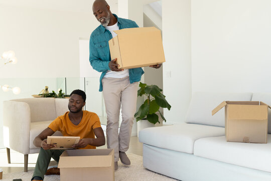Unpacking African American family inspecting moving boxes in home living room, with framed picture