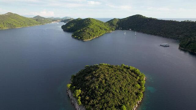 Aerial view of a lush green isle surrounded by calm, deep blue waters, framed by distant, wooded islands, Elaphiti islands, Dalmatian Coast, Dubrovnik-Neretva County, Croatia.