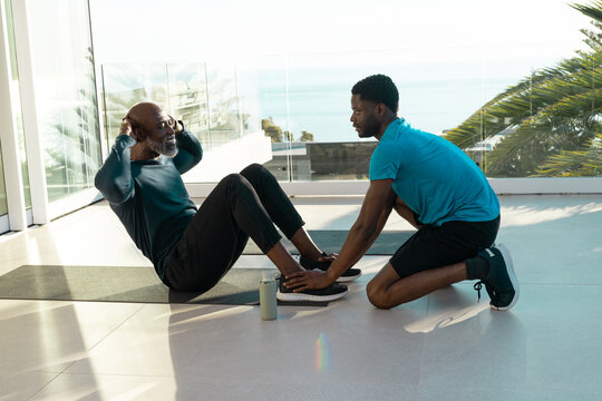 Senior African American man and African American trainer doing sit-ups in gym, with sliding discs