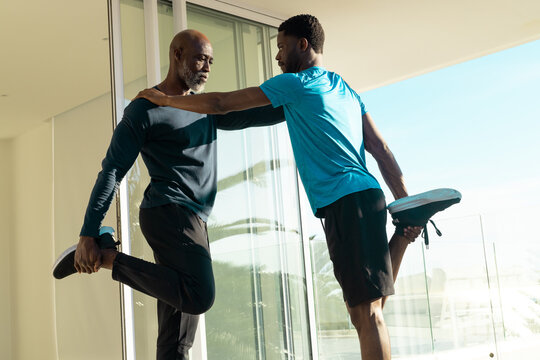 African American personal trainer and senior client stretching quads on balcony, wearing sneakers