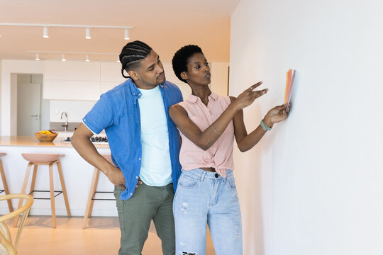 Standing diverse couple examining paint swatch cards in open-plan kitchen, with fruit bowl