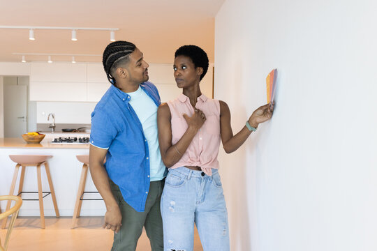 Choosing paint colors, Diverse couple standing in modern kitchen, with swatches against blank wall