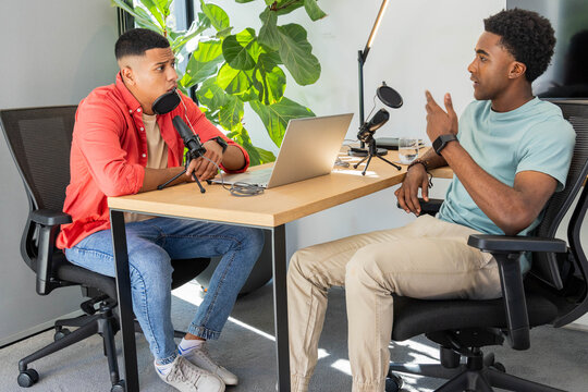 Diverse coworkers recording podcast episode in studio corner, with microphones and laptop