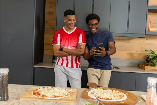 Leaning Diverse male friends against marble countertop in modern home kitchen, with uncooked pizzas