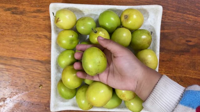 hand holding fresh green ber fruit over bowl of jujube on wooden table healthy seasonal fruit