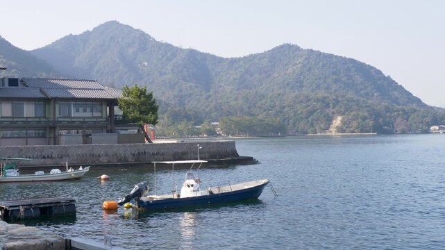 Slow motion landscape of boat docked at jetty harbour inlet along coastal bay at Mikasa beach with Misen mountain forest in the background of Hatsukaichi town Miyajima Island Hiroshima Japan tourism
